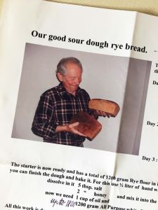An older man holding two loaves of no knead sourdough rye bread