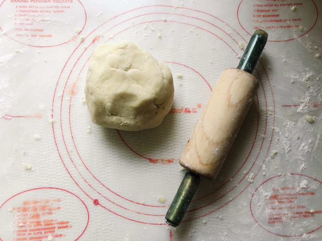 A ball of German Plum Spelt Cake (Pflaumenkuchen mit Mürbeteig) dough and small rolling pin on a baking mat