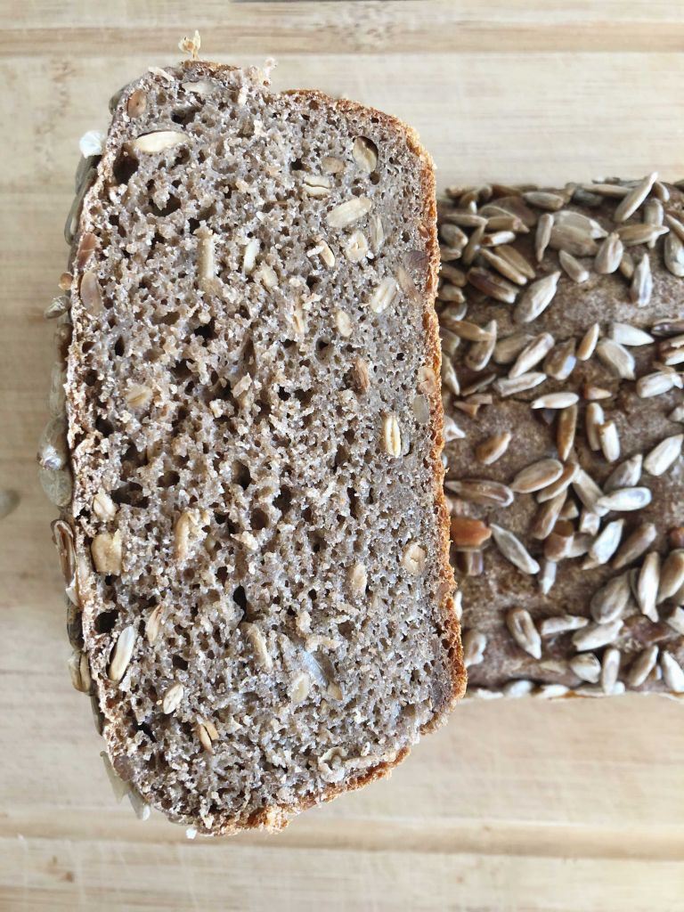 A loaf of whole grain rye sourdough bread sliced in half with with one half facing upwards to show the inside texture