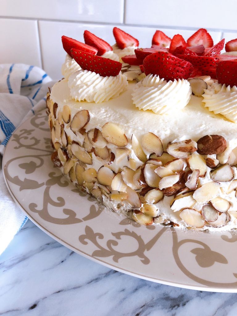 The side of a german buttercream spelt torte covered with sliced almonds and topped with swirls of buttercream and strawberries