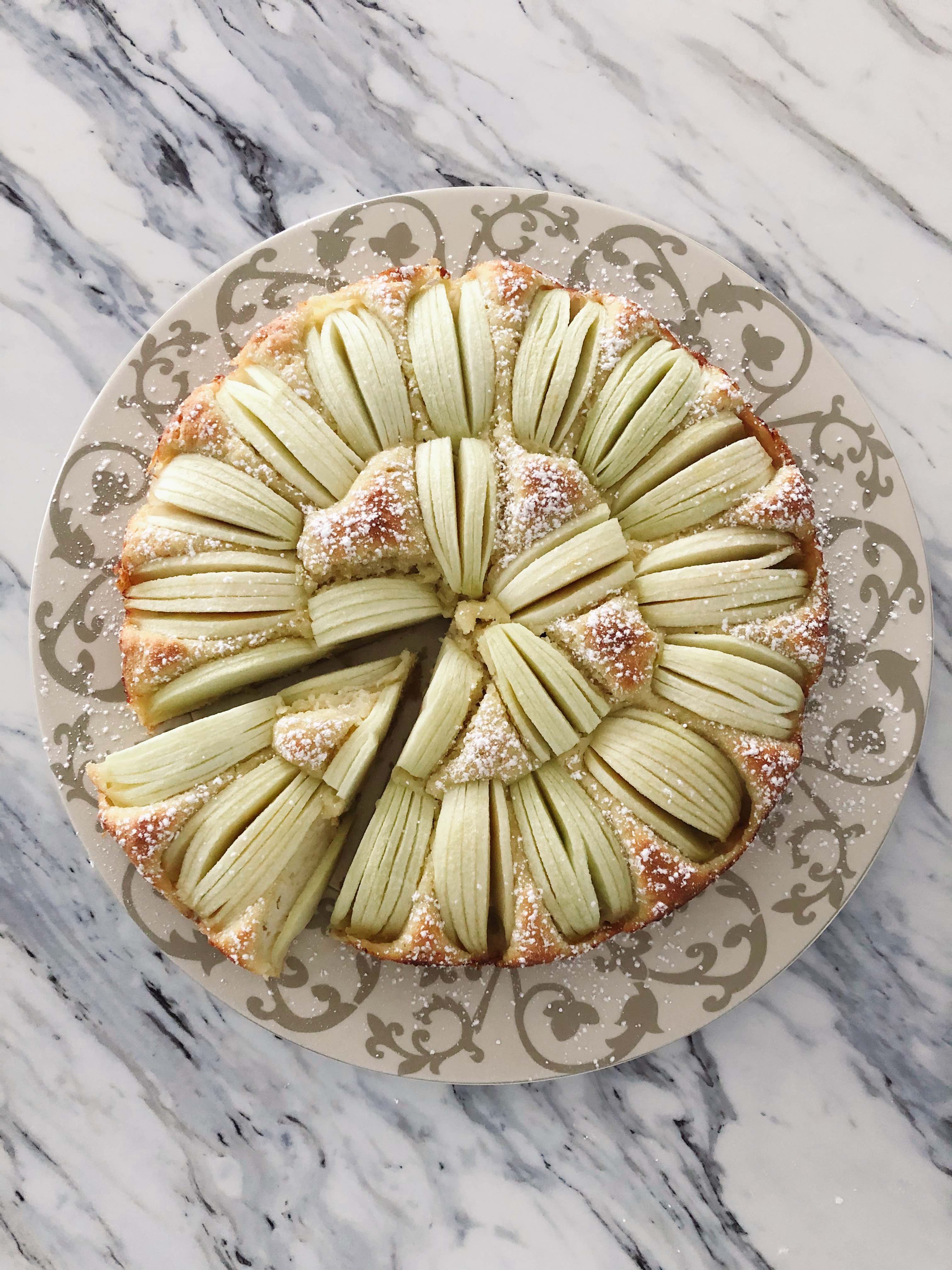 An apple sponge cake made with spelt flour on a decorative plate with one slice cut
