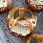 Close up of one deep brown german schwabisch style pretzel cooling on a wire rack with other pretzels around it.