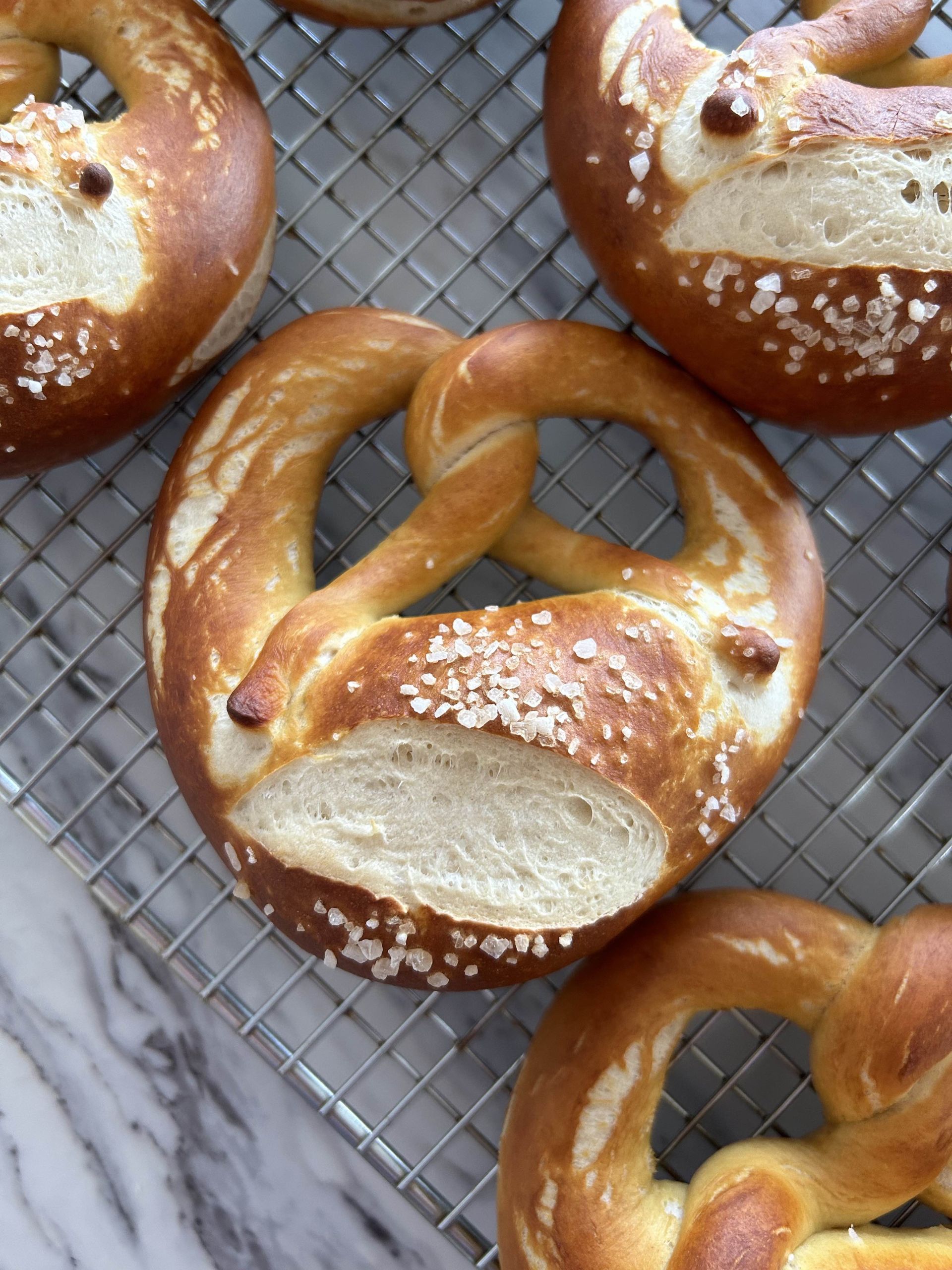 Close up of one deep brown german schwabisch style pretzel cooling on a wire rack with other pretzels around it.