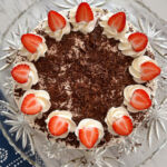 German strawberry cream torte on a decorative glass plate sitting on a marble looking countertop