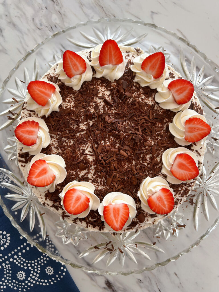 German strawberry cream torte on a decorative glass plate sitting on a marble looking countertop
