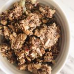 A small white bowl filled with nutty granola clusters on a white countertop