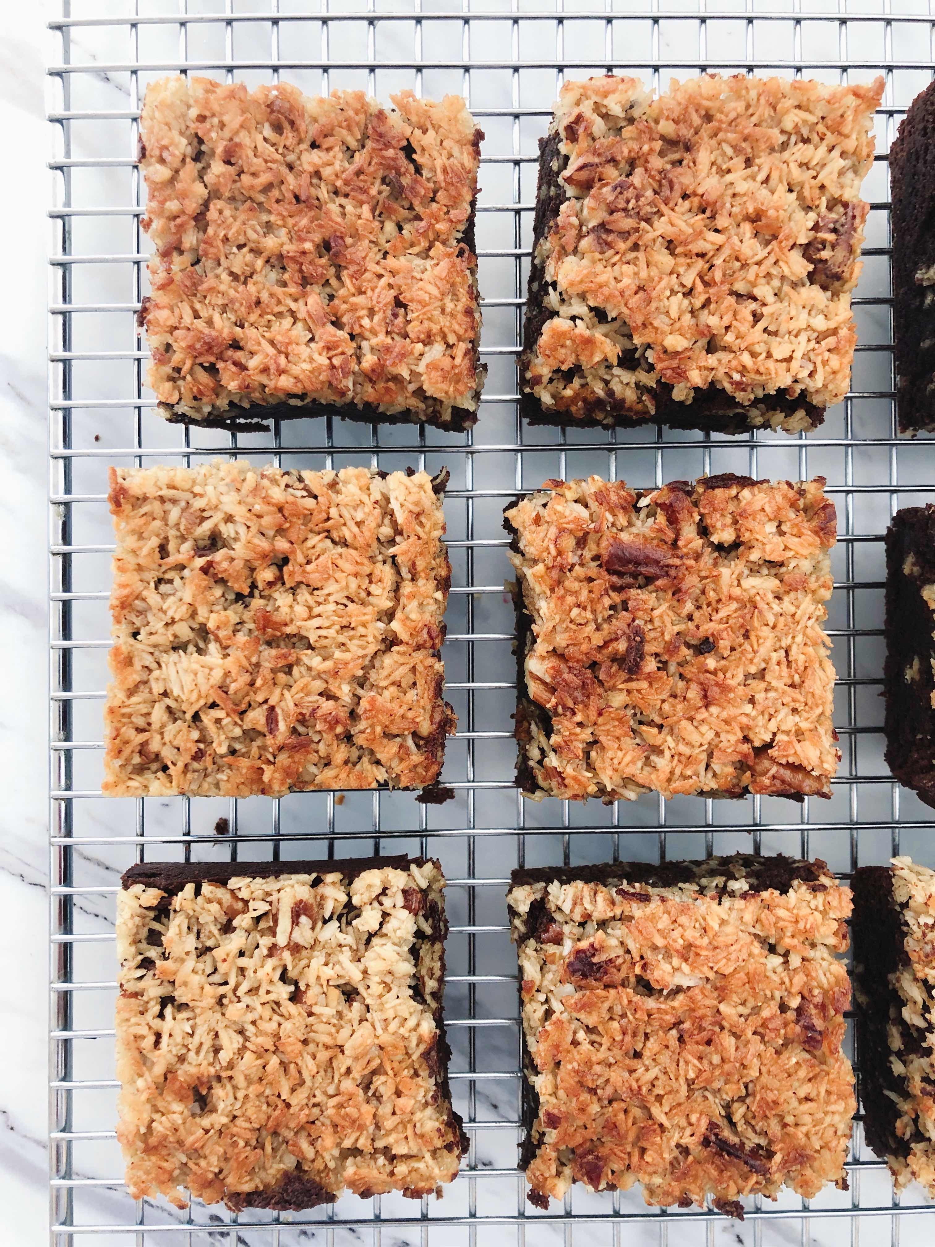 Six A pile of Whole Grain Rye Brownies with Toasted Coconut Pecan Topping lined up side by side on a cooling rack