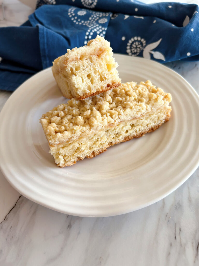 Two slices of spelt strueselkuchen on a white plate with a blue and white tea towel in the background