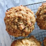 Close up of one lemon rhubarb spelt muffin with streusel on top surrounded up two other muffins all cooling on a wire rack