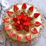 Top down view of a german buttercream spelt torte covered with sliced almonds and topped with swirls of buttercream and strawberries