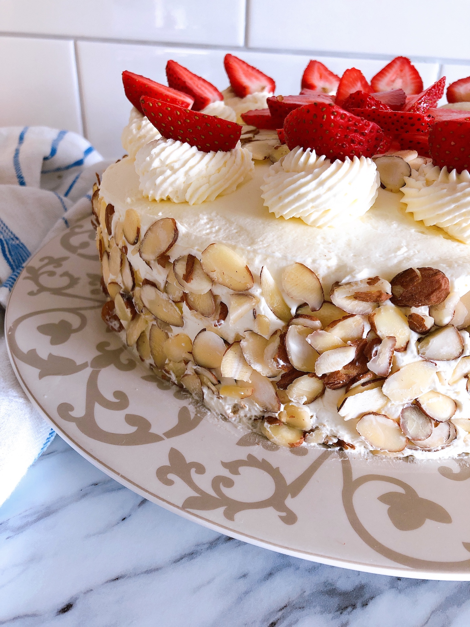 The side of a german buttercream spelt torte covered with sliced almonds and topped with swirls of buttercream and strawberries