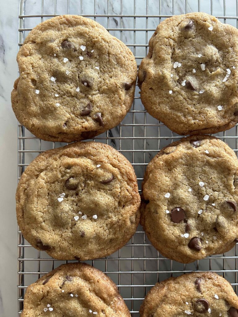 Four browned butter and chocolate chip cookies with a little bit of course salt sprinkled on top of each cooling on a wire rack.