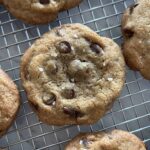 Close up of one browned butter and rye chocolate chip cookie with a little bit of course salt sprinkled on top cooling on a wire rack.