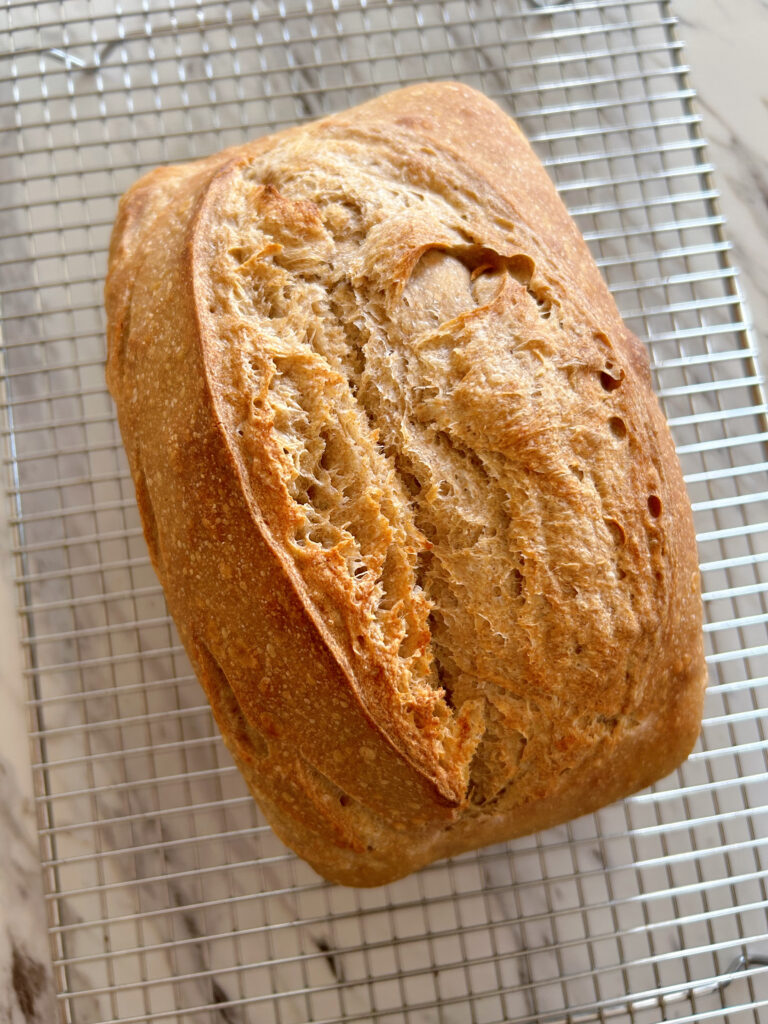 One golden brown wheat, spelt and rye sourdough pan loaf cooling on a wire rack.