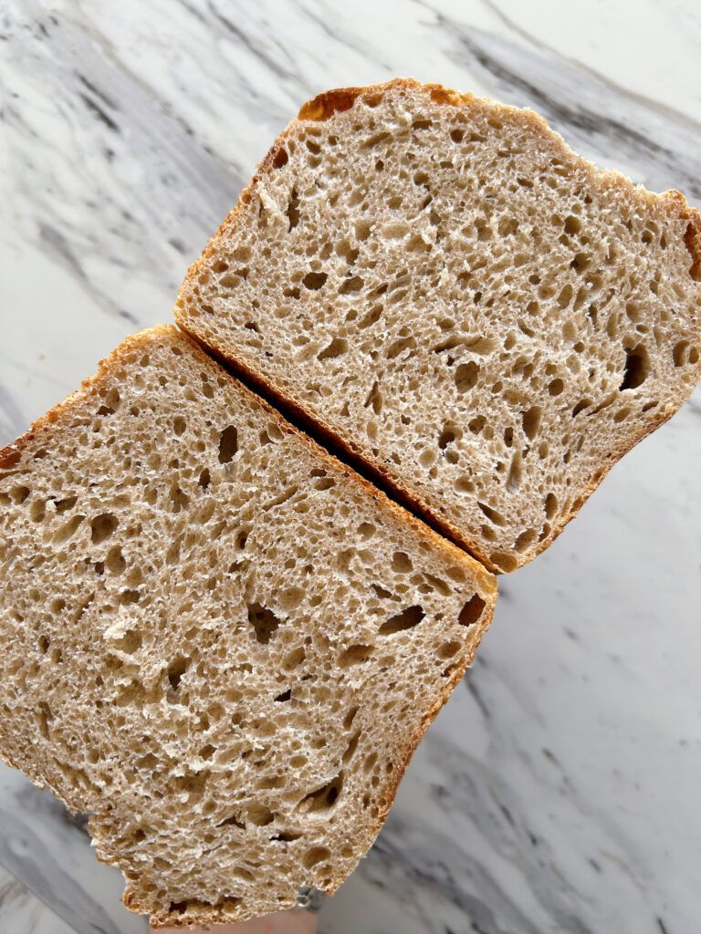 One wheat, spelt and rye sourdough pan loaf sliced down the middle, opened and held bottom to bottom showing the airy but uniform interior crumb.