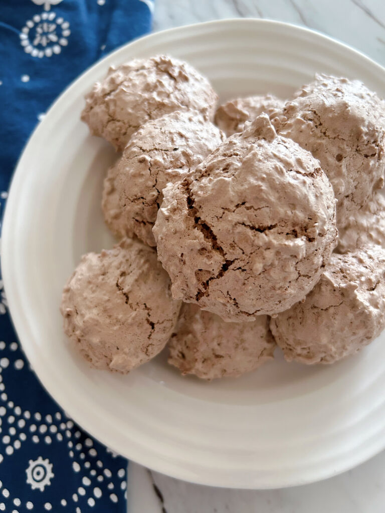 Eight german chocolate coconut macaroons (raspeli) piled on top of each other on a small white plate with a deep blue tea towel in the background.