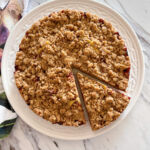 Close up of a round plum streusel cake with one slice made and pulled slightly away from the rest of the cake.