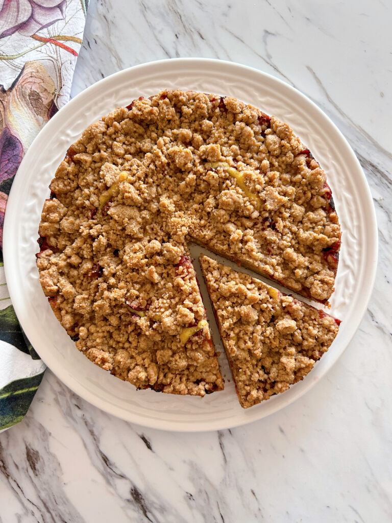 Close up of a round plum streusel cake with one slice made and pulled slightly away from the rest of the cake.